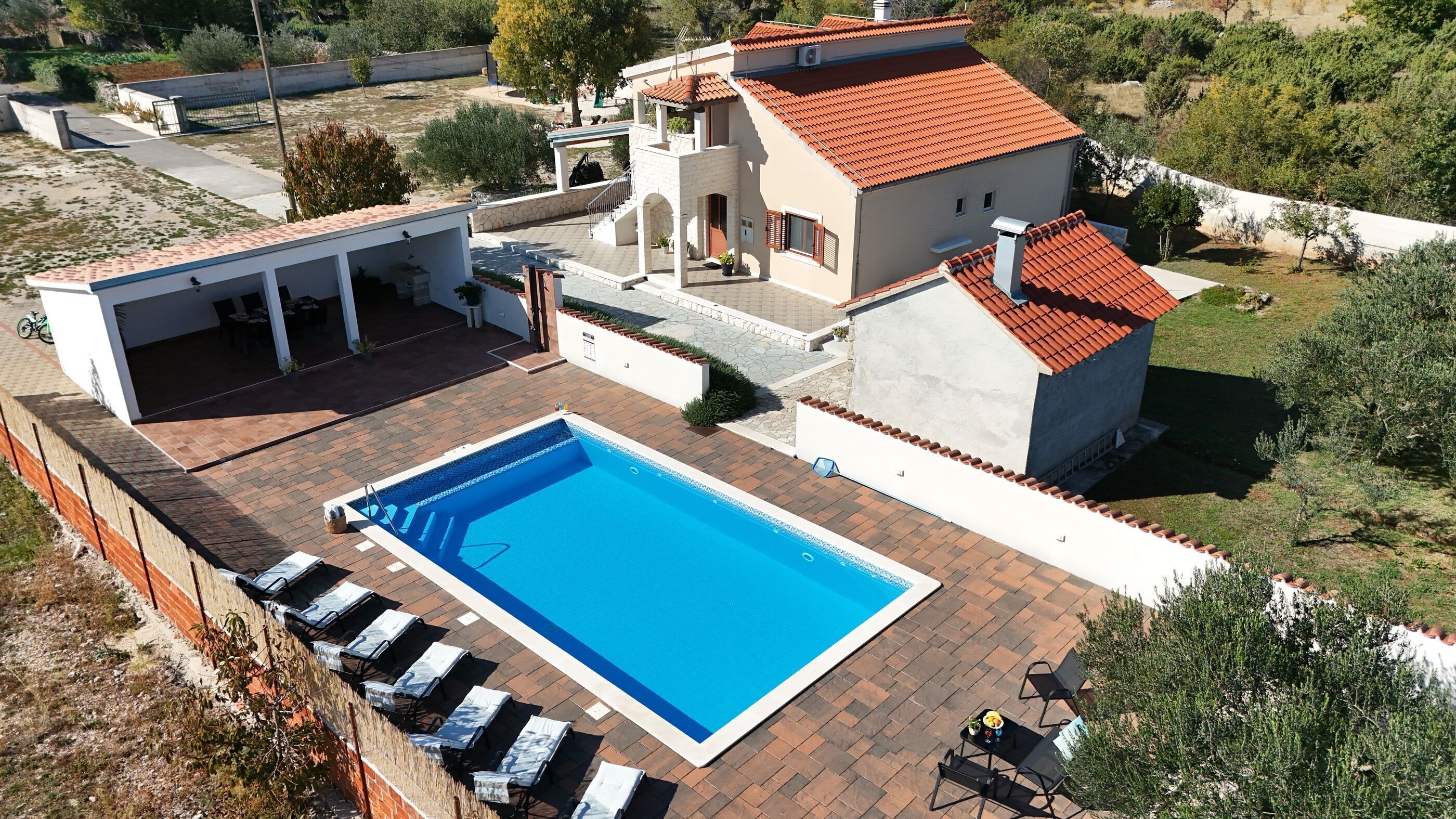 A residential property with a swimming pool, outdoor seating, and a covered patio area.