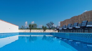 Una piscina azul clara con bordes de azulejos, rodeada de sillas de descanso y un muro de piedra.