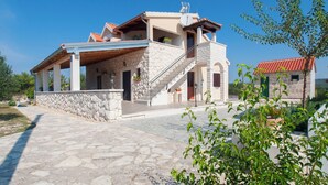 Una casa de piedra de dos pisos con un balcón, un muro de piedra y un techo de tejas rojas.