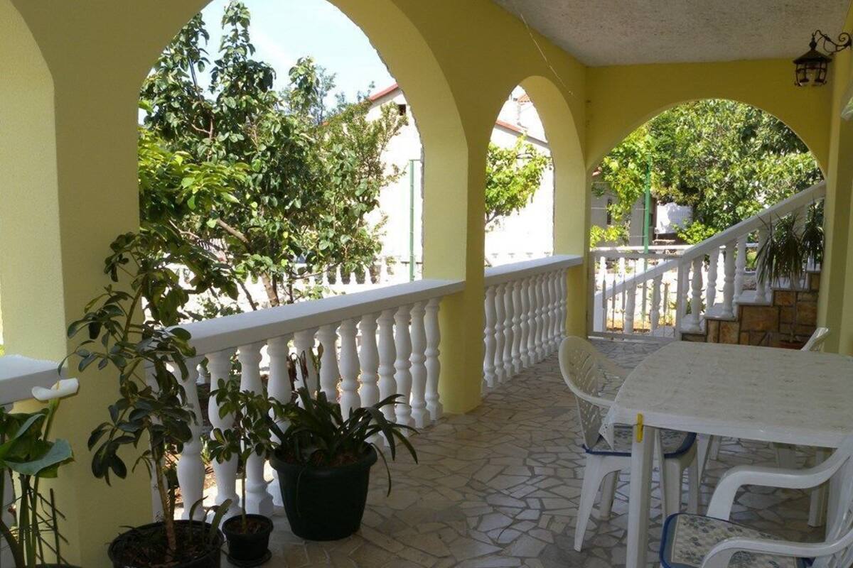 Een terras buiten met witte stoelen en een tafel, omgeven door gele muren en witte leuningen.