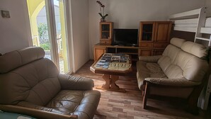 Un soggiorno con due divani in pelle, un tavolino da caffè con riviste, una TV, armadietti in legno e un condizionatore d'aria.