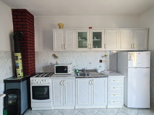 Een keuken met witte kasten, een gasfornuis, een magnetron, een koelkast en een bakstenen schoorsteen.