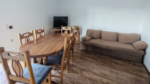 Un soggiorno con un tavolo da pranzo in legno, sei sedie, un divano beige e un televisore su un mobile.