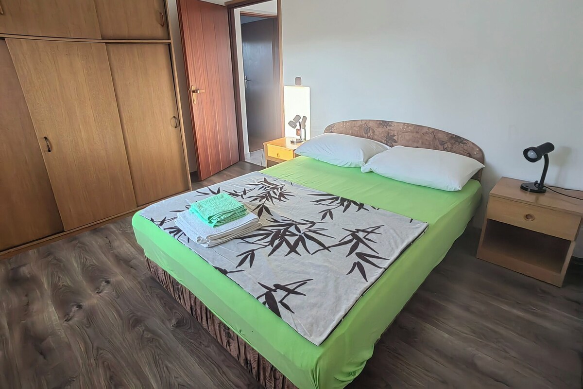 Een slaapkamer met een bed, een nachtkastje, een kledingkast en een deur naar een andere kamer.