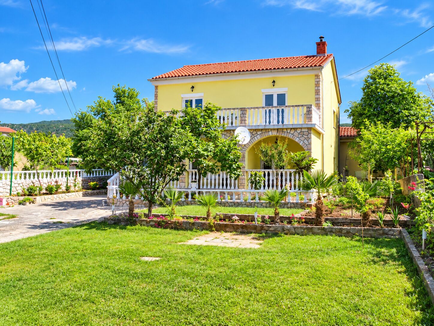 A two-story yellow building with a red-tiled roof, a white fence, and a well-maintained lawn.