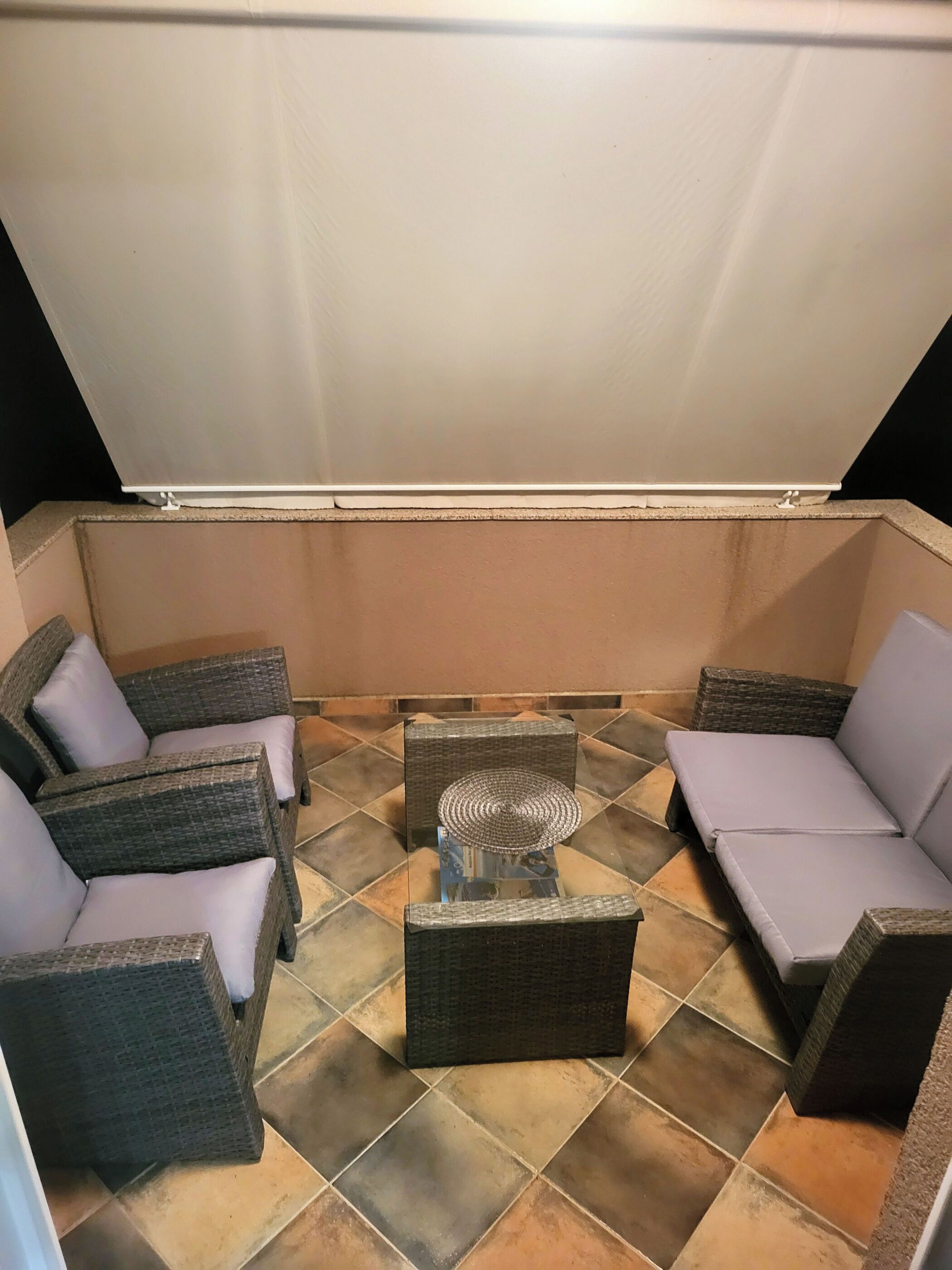 A covered patio area with wicker furniture and a glass-top table.