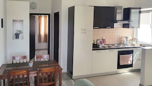 A compact living space with a dining area, kitchenette, and a green sofa. - Apartments Mirko i Jela (Nin)