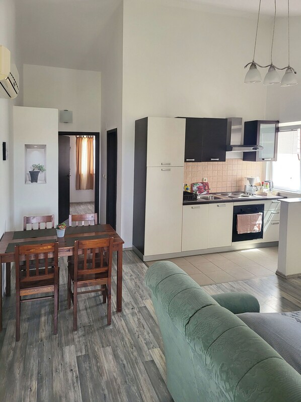 A compact living space with a dining area, kitchenette, and a green sofa. - Apartments Mirko i Jela (Nin)