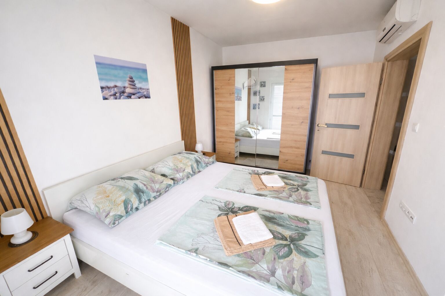 A bedroom with a bed, bedside table, nightstand, wardrobe, and a mirror.