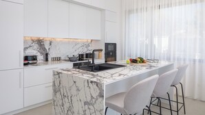 Een moderne keuken met witte kasten, een marmeren eiland en een ingebouwde oven.