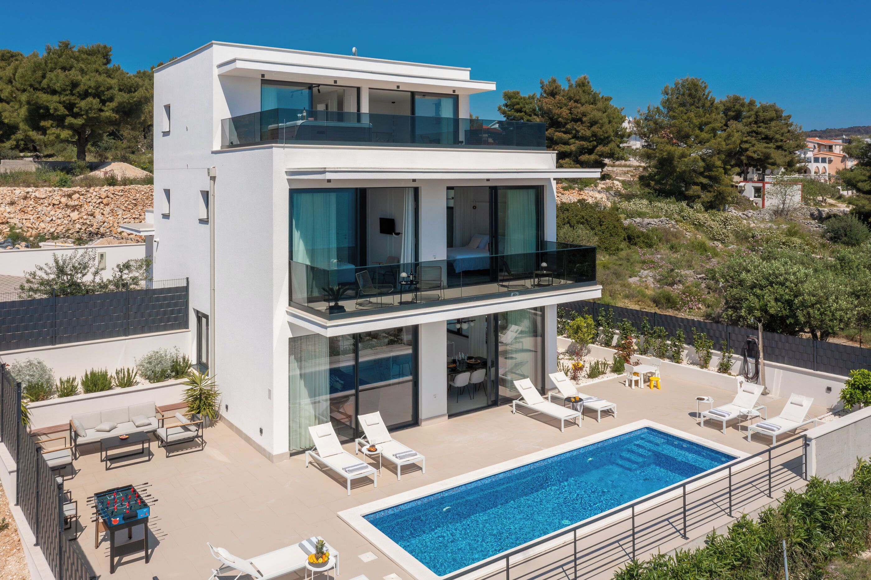 A modern two-story house with a swimming pool, outdoor seating, and a balcony.