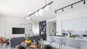 Een moderne keuken met een marmeren aanrecht, een eetgedeelte met een houten tafel gedekt voor zes personen, en een zithoek met een grijze bank en een flatscreen-tv.