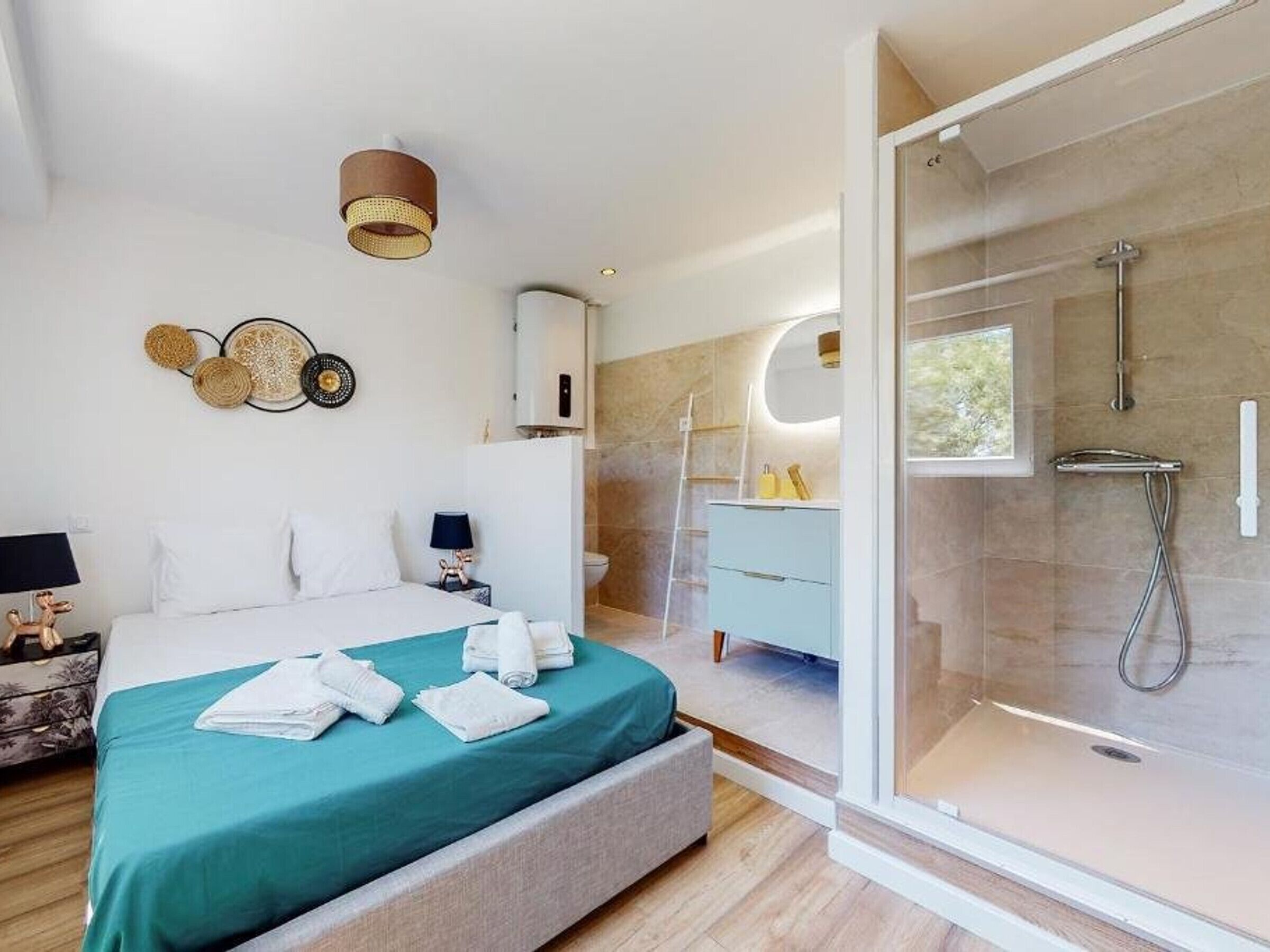 A modern bedroom with a bed, bedside tables, a nightstand, a bathroom with a shower, and a glass door leading to the shower area.