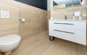 A modern bathroom with a toilet, a sink with a mirror, and a towel dispenser. - Villa Delux View (Slivno)