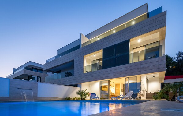 A modern multi-story house with a swimming pool, outdoor seating, and a well-lit interior. - Villa Delux View (Slivno)
