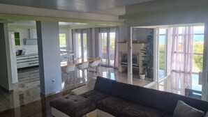 A spacious living area with a large sofa, a dining table with chairs, and a kitchen area visible through an open door. - Villa Arres (Kastela)