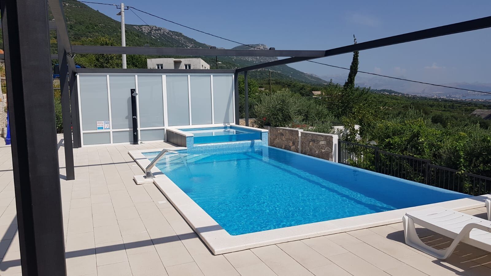 Una piscina rectangular con un jacuzzi pequeño, rodeada por un deck blanco y una pérgola.