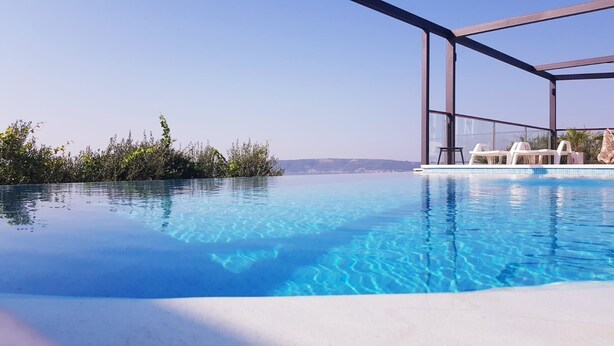 A clear blue infinity pool with a view of the sea and a modern outdoor seating area. - Villa Arres (Kastela)