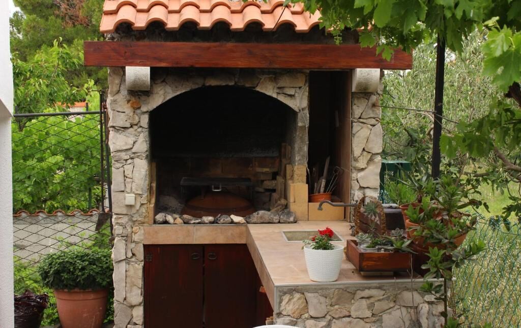 A stone-built outdoor oven with a tiled roof, surrounded by potted plants and a stone wall.