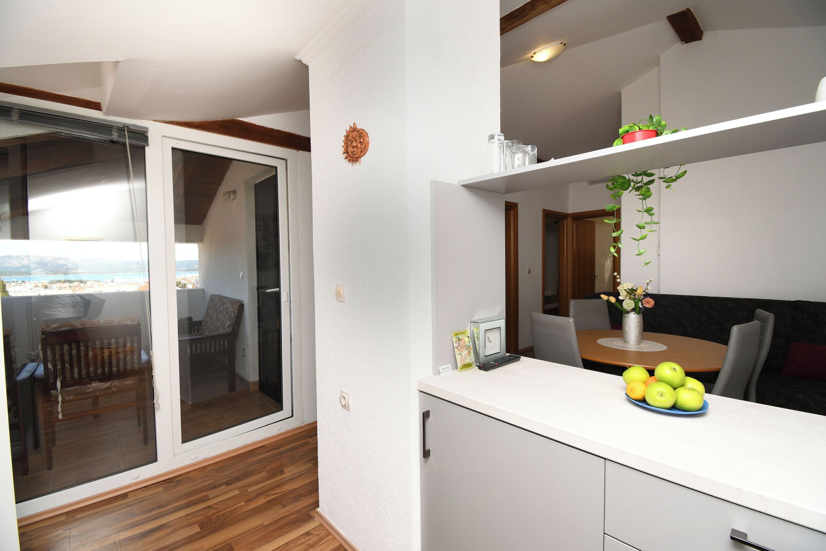 Une cuisine moderne avec un coin repas, une porte-fenêtre coulissante donnant sur un balcon et une petite plante posée sur le plan de travail.