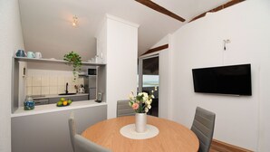 A dining area with a round wooden table, grey upholstered chairs, a white vase with flowers, and a TV mounted on the wall. - Apartments Family Villaarta (Murter-Kornati)