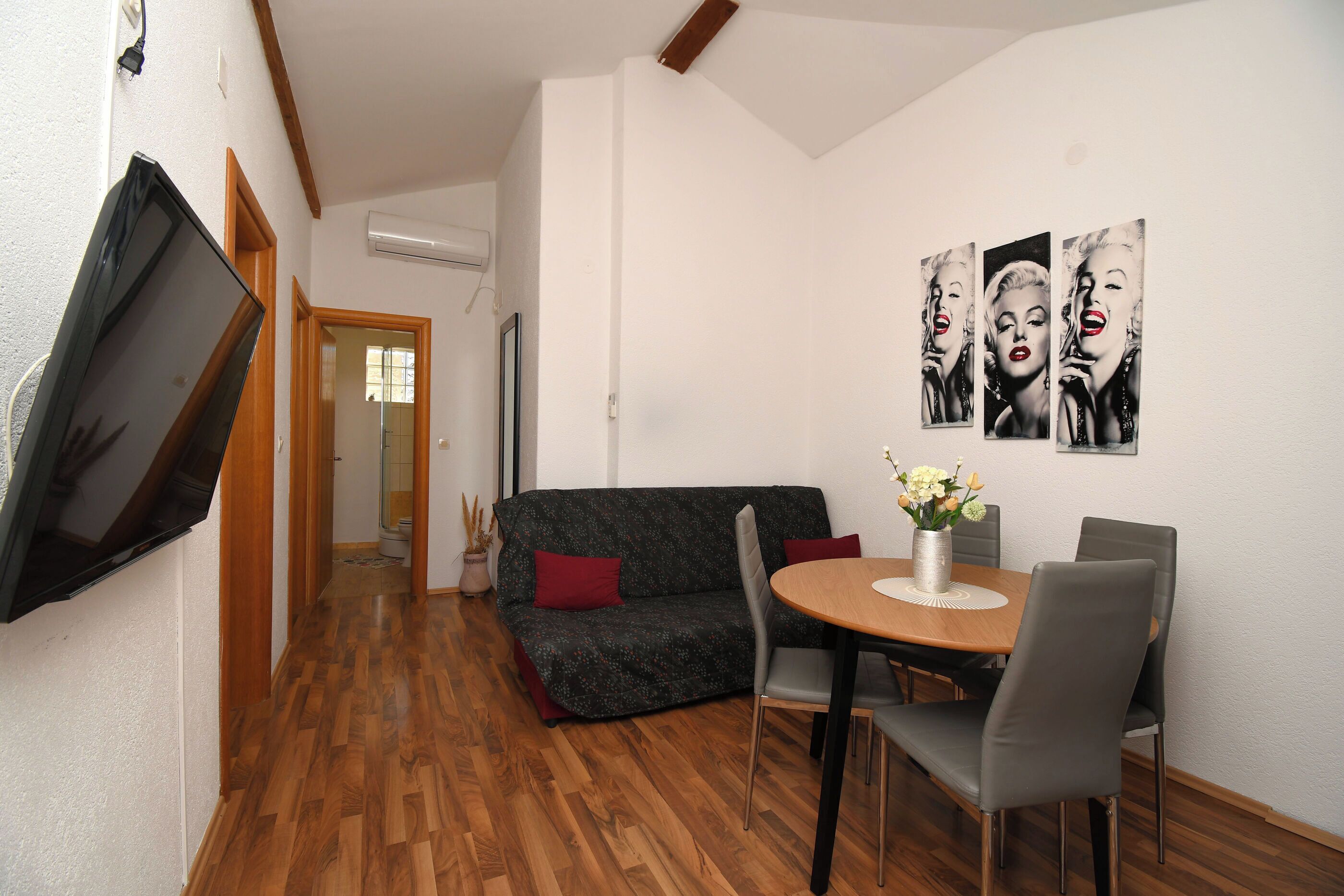 Una sala de estar con un sofá, una mesa de comedor con sillas y un televisor montado en la pared.
