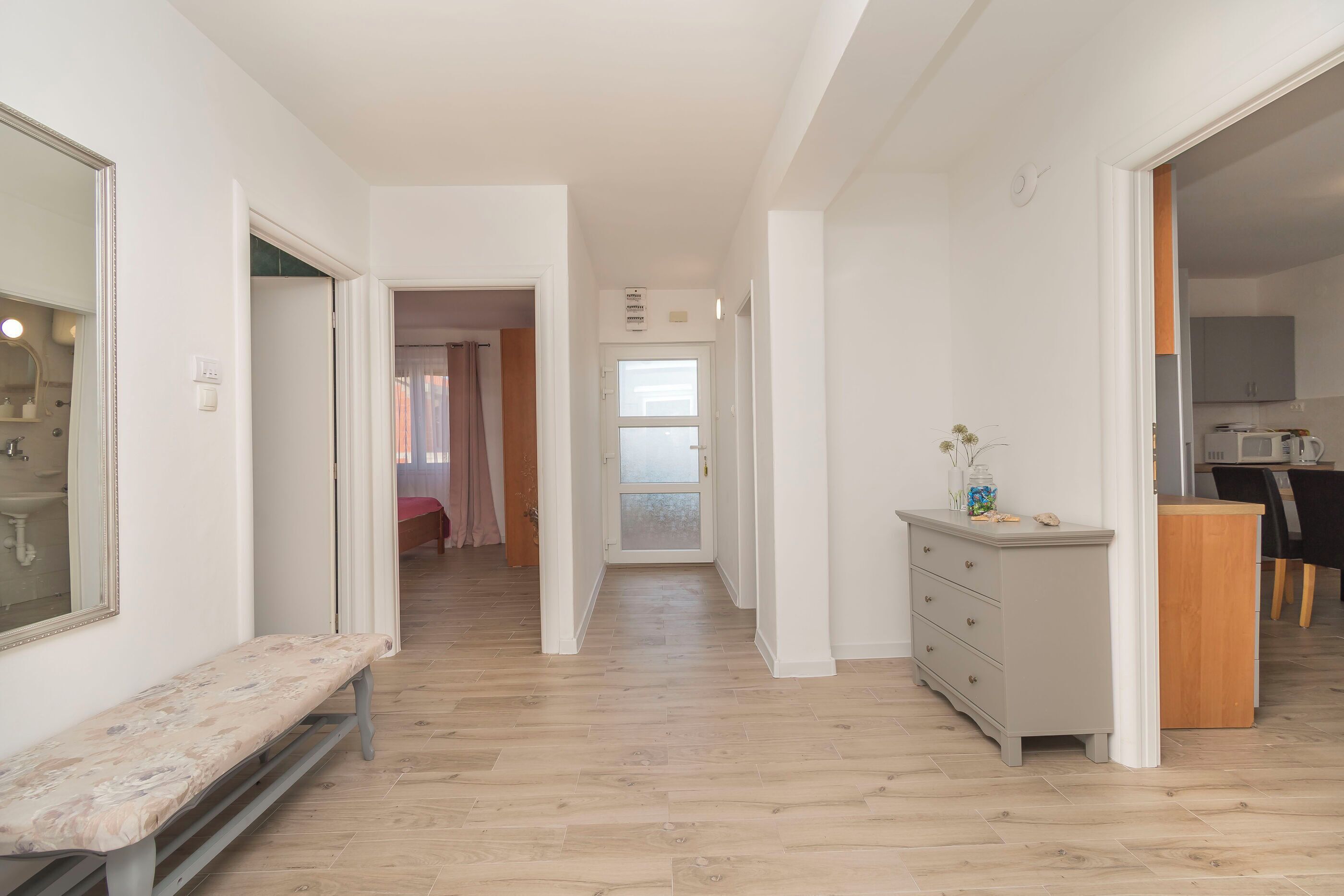 A narrow hallway with a bench, a dresser, and a door leading to a room with a shower.