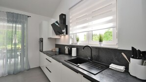 A modern kitchen with a black sink, white cabinets, and a window with blinds. - Villa Tersaz (Sveta Nedelja)