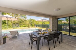 A modern outdoor patio with a pool, dining table, chairs, and umbrellas. - Villa Tersaz (Sveta Nedelja)