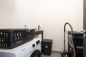 A compact washer and dryer unit with a basket on top, a small trash bin, and a vacuum cleaner. - Villa Tersaz (Sveta Nedelja)