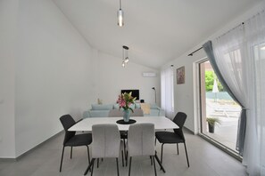 A modern dining area with a white table, four chairs, a vase with flowers, and a hanging light fixture. - Villa Tersaz (Sveta Nedelja)