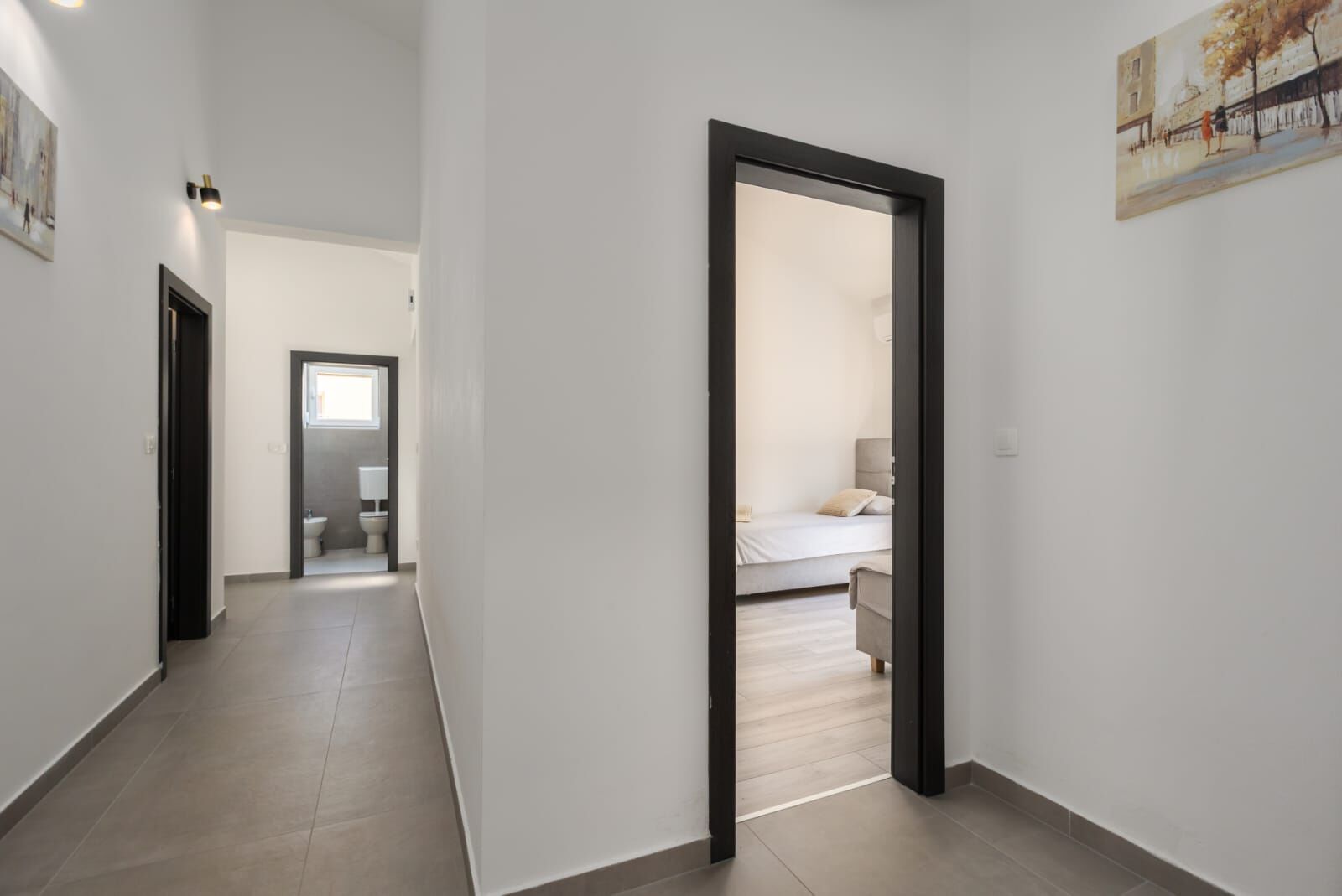 A hallway leading to a bedroom with a bed, a chair, and a painting on the wall.