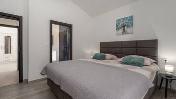 Quarto com cama, mesa de cabeceira, quadro e porta que dá para outro cômodo.