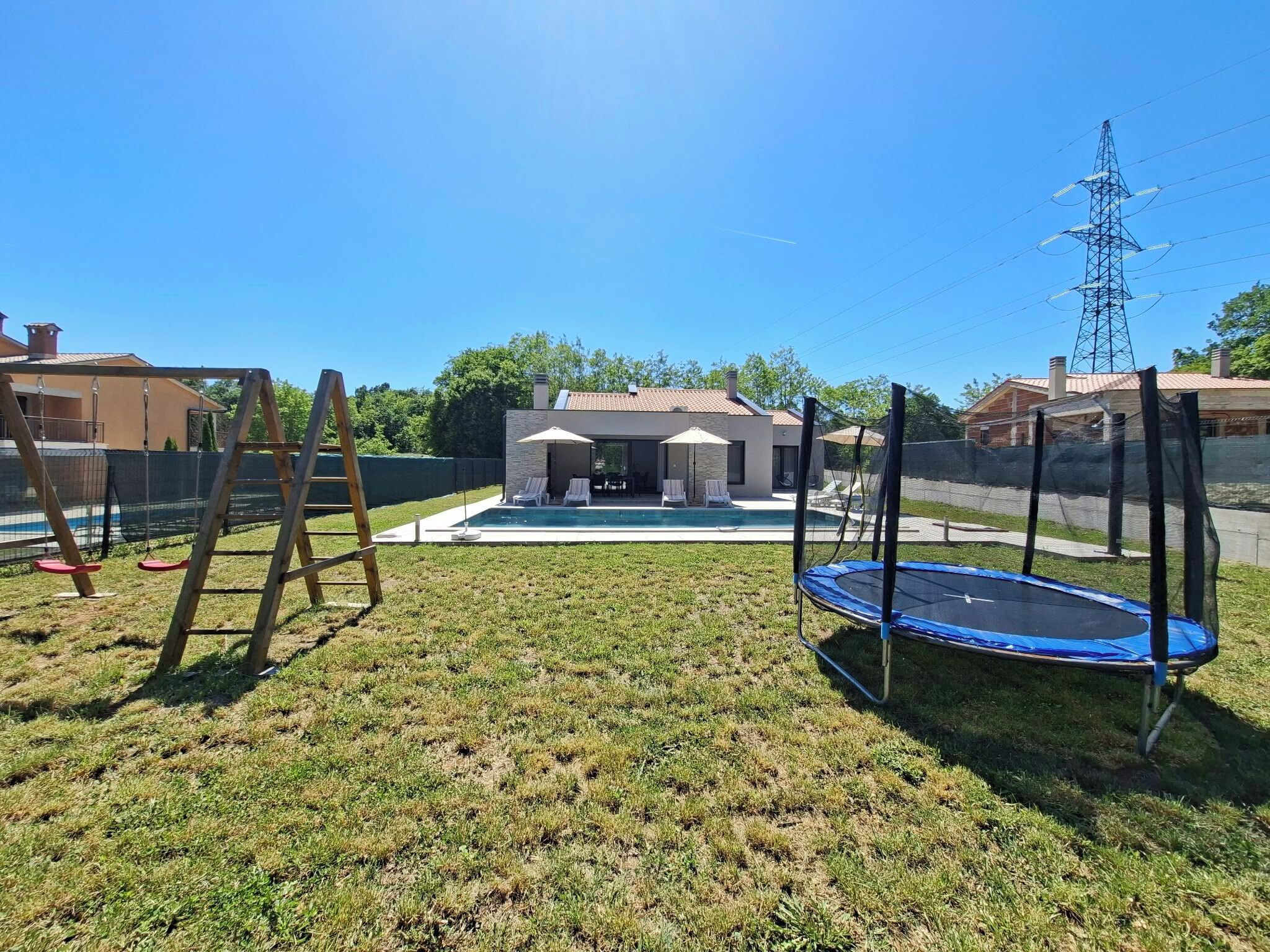 Um quintal com trampolim, balanço e área de piscina.