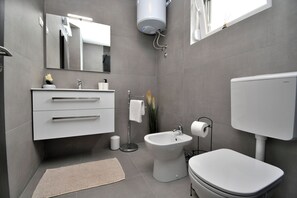 A modern bathroom with a white vanity, bidet, toilet, and a large mirror. - Villa Tersaz (Sveta Nedelja)