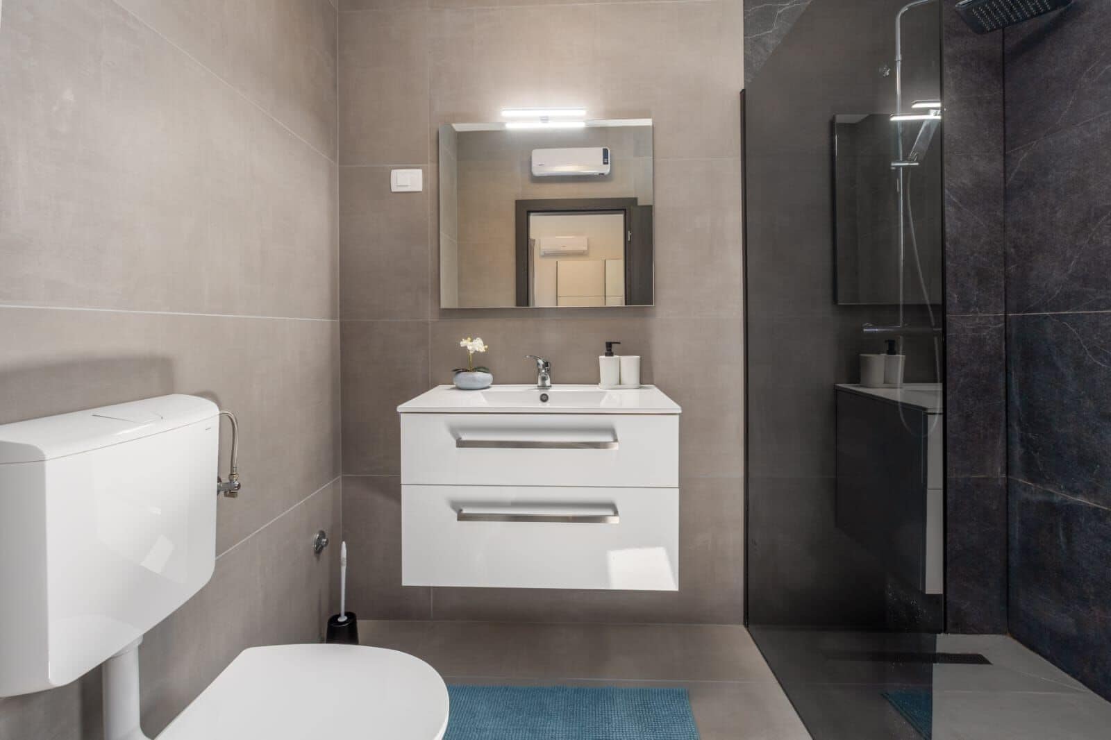 A modern bathroom with a toilet, a sink with a mirror, and a shower area.