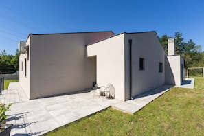 A modern building with a flat roof, a small patio area with a table and chairs, and a chimney. - Villa Tersaz (Sveta Nedelja)