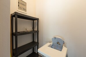 Egy szoba sarka, ahol egy fekete polcrendszer, egy fehér szék és egy keretezett kép található a falon.