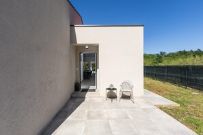 A modern outdoor patio with a concrete floor, a metal chair, a small round table, and a potted plant. - Villa Tersaz (Sveta Nedelja)