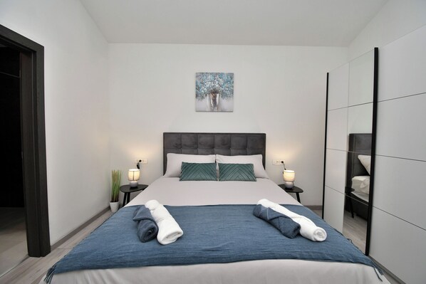 Ein modernes Hotelzimmer mit einem großen Bett, zwei Nachttischen inklusive Lampen, einem Bild an der Wand und einem Kleiderschrank.