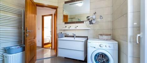 A modern bathroom with a washing machine, a sink, and a mirror.