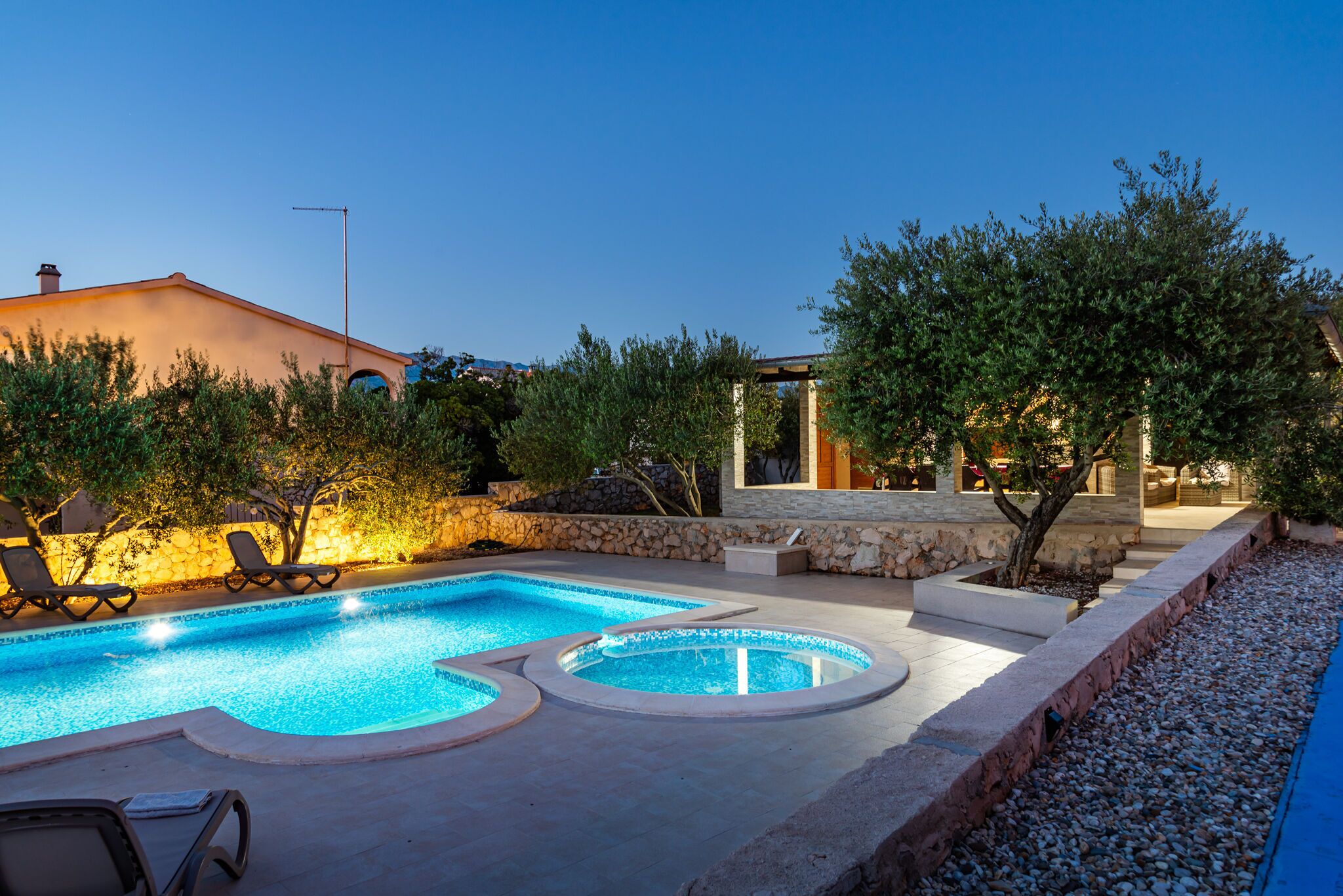 A swimming pool with lounge chairs, a stone wall, and a pergola.