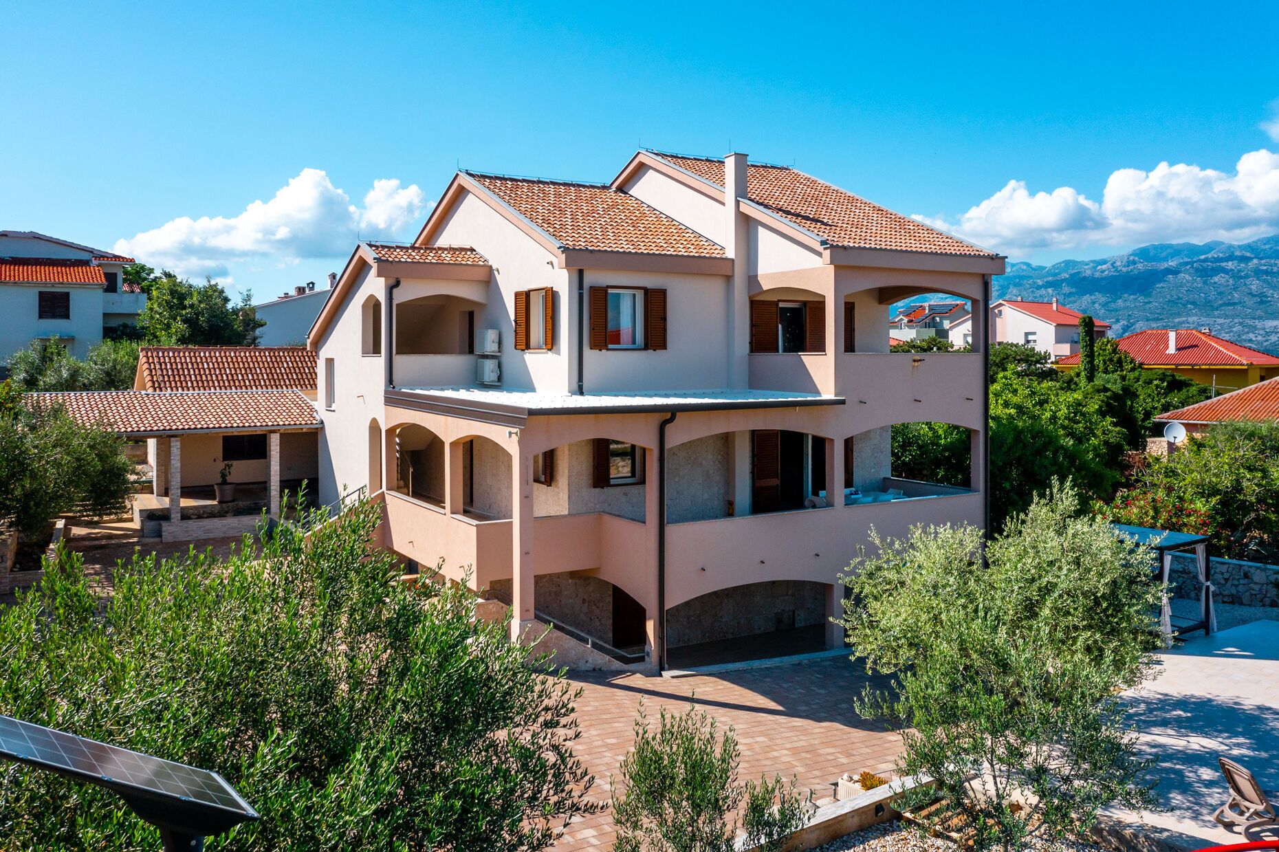 A multi-story house with a tiled roof, balconies, and a paved courtyard.