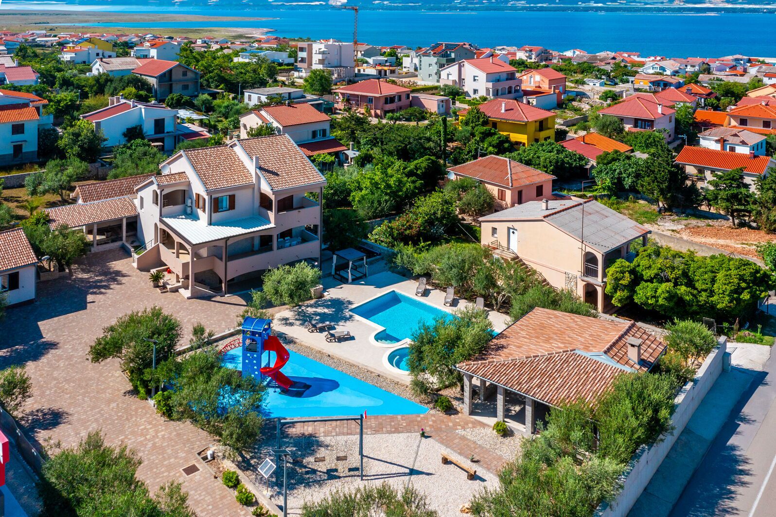 An aerial view of a coastal residential area with houses, a swimming pool, and a water slide.