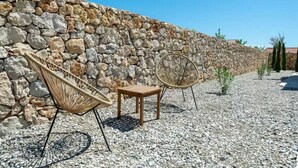 A stone wall with wicker chairs and a small wooden table in a pebbled area. - Villa St Vid 4 (Privlaka)