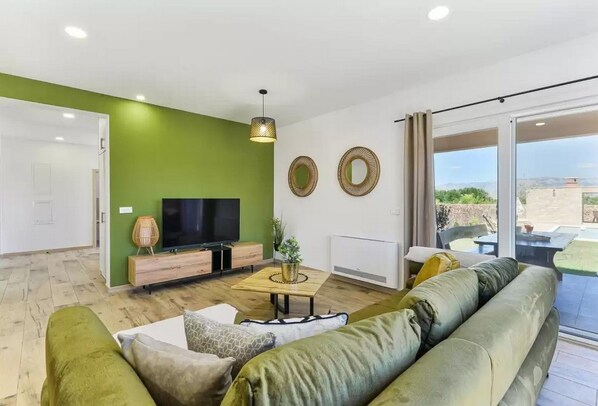 A modern living room with a green accent wall, a flat-screen TV, a wooden coffee table, and a large green sofa. - Villa St Vid 4 (Privlaka)