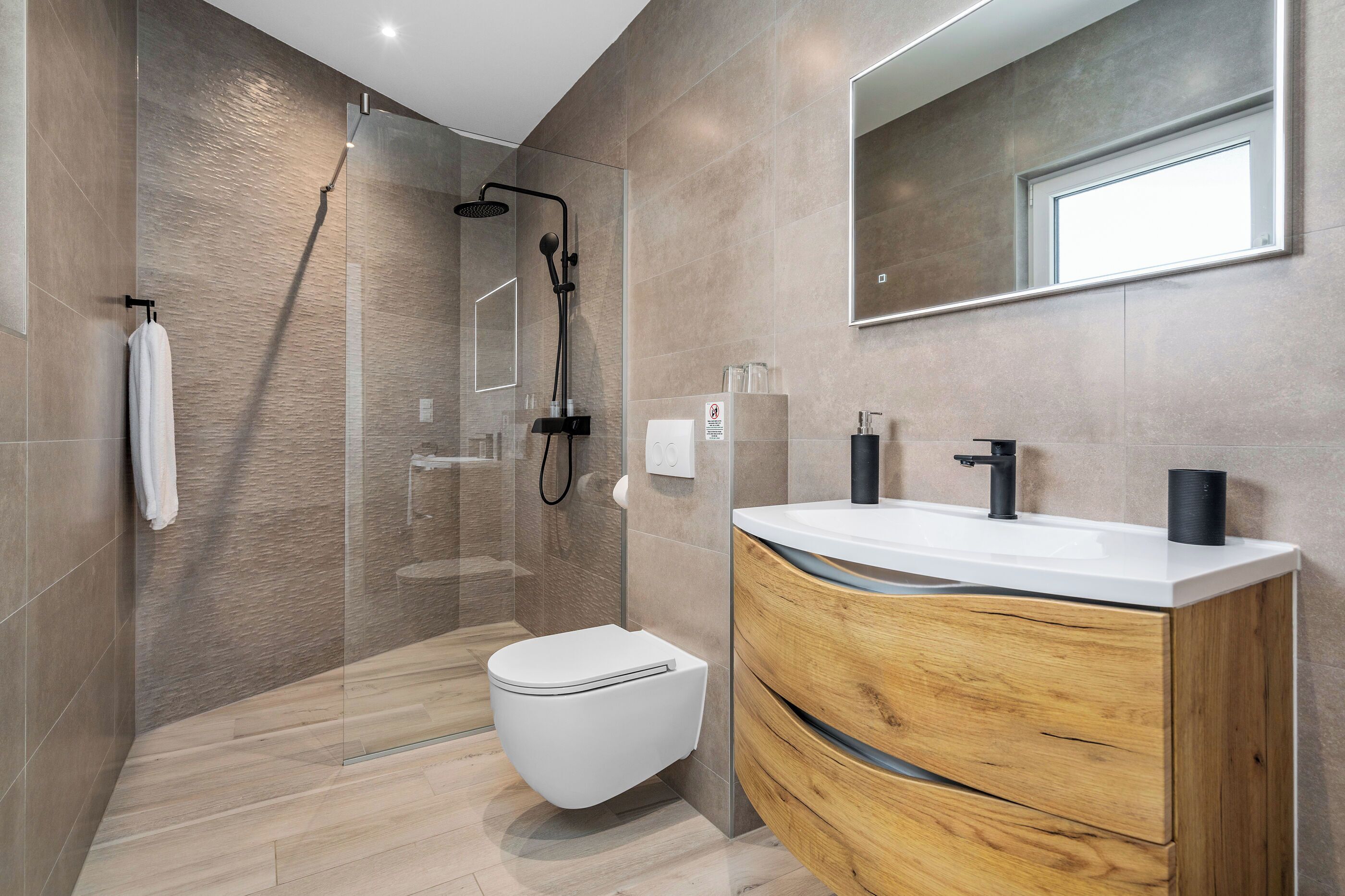 A modern bathroom with a glass-enclosed shower, a white toilet, and a wooden vanity with a sink.