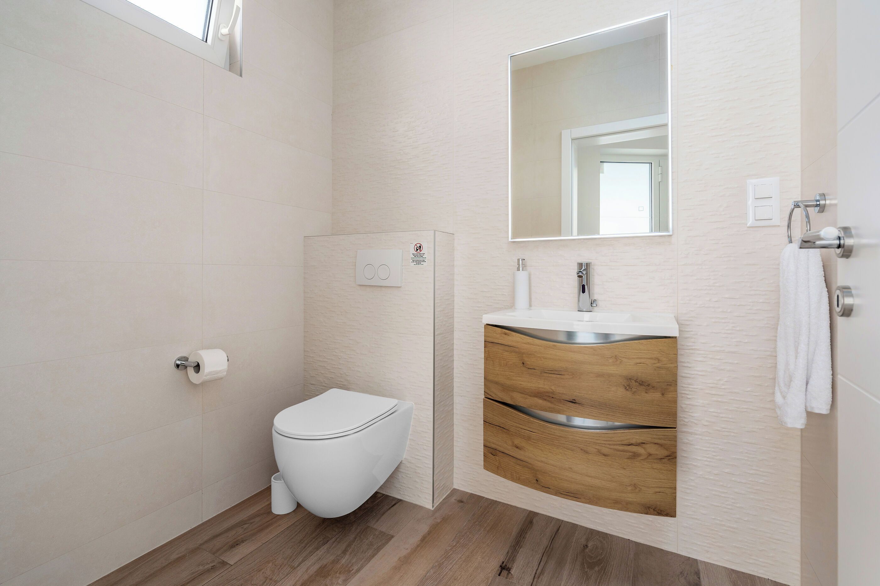 A modern bathroom with a toilet, a sink with a wooden vanity, and a mirror above the sink.