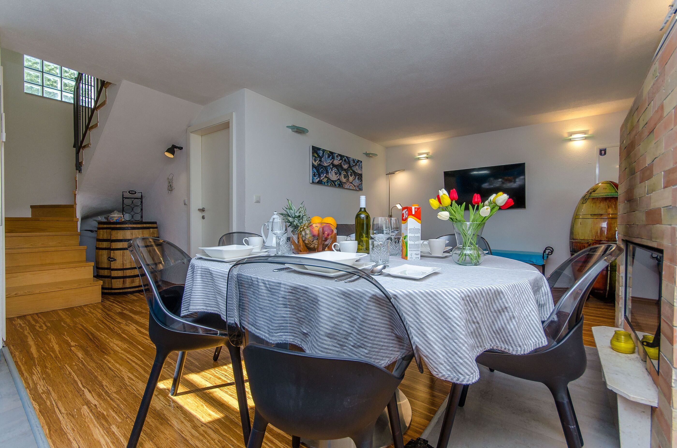 A dining area with a table set for four, a vase with flowers, and a staircase in the background.