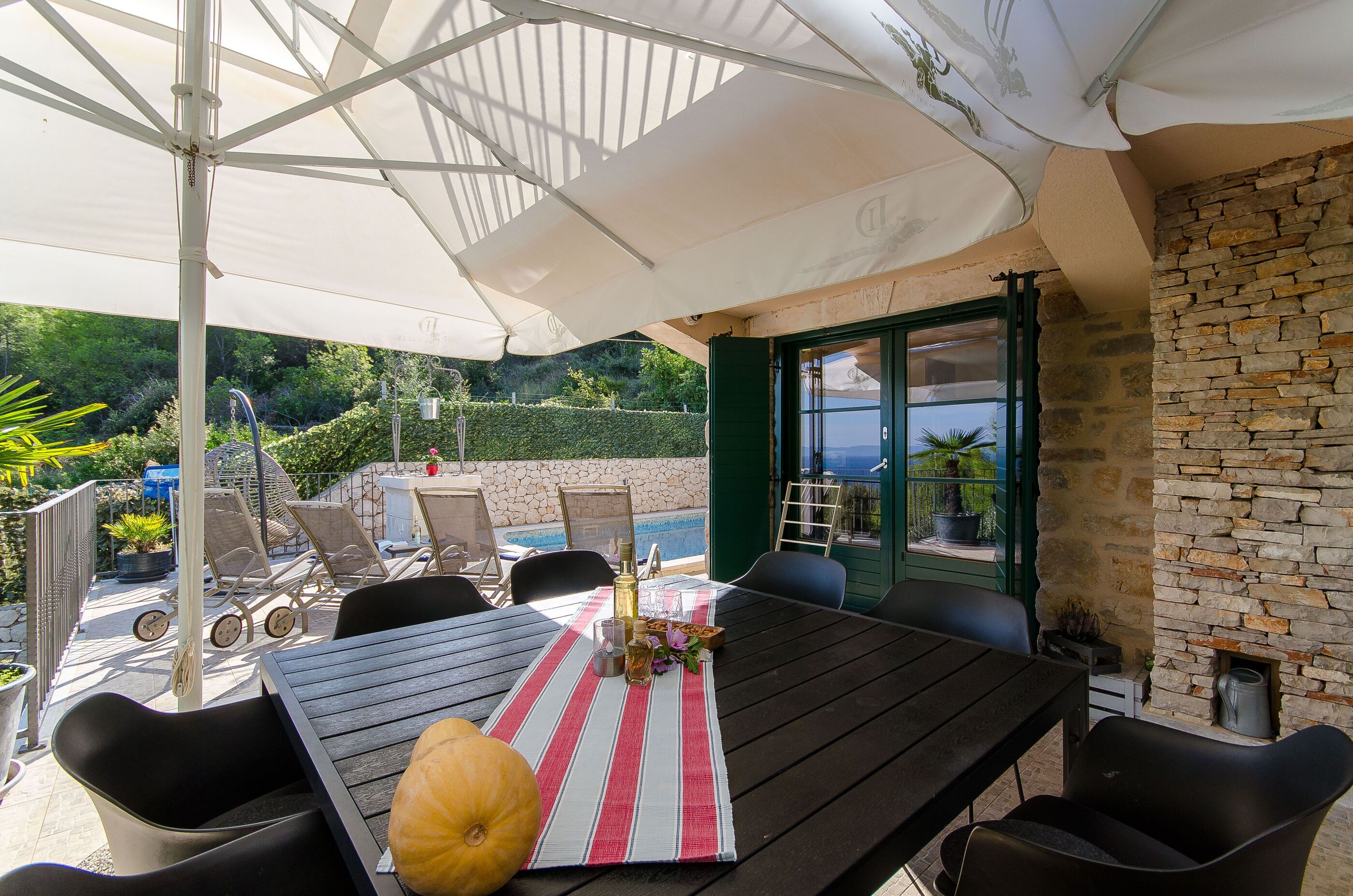 Een terras buiten met een eettafel, omringd door stoelen, onder een grote parasol.